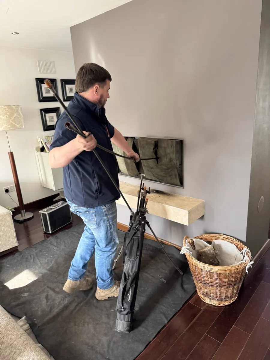Johnny Roberts sweeping a chimney with rods in a sitting room, dust sheet on the floor