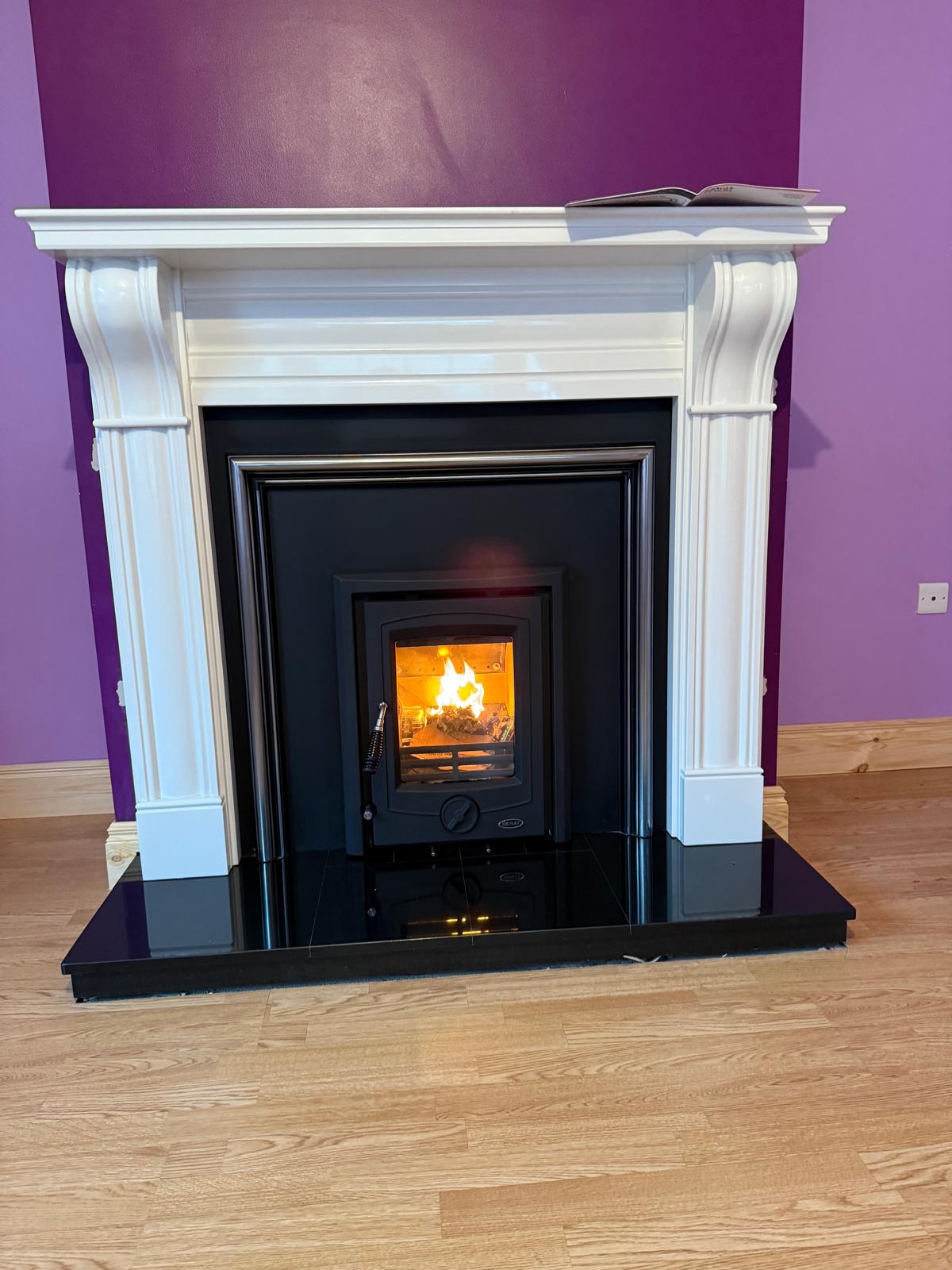 White fluted surround stove with fire lit against purple wall